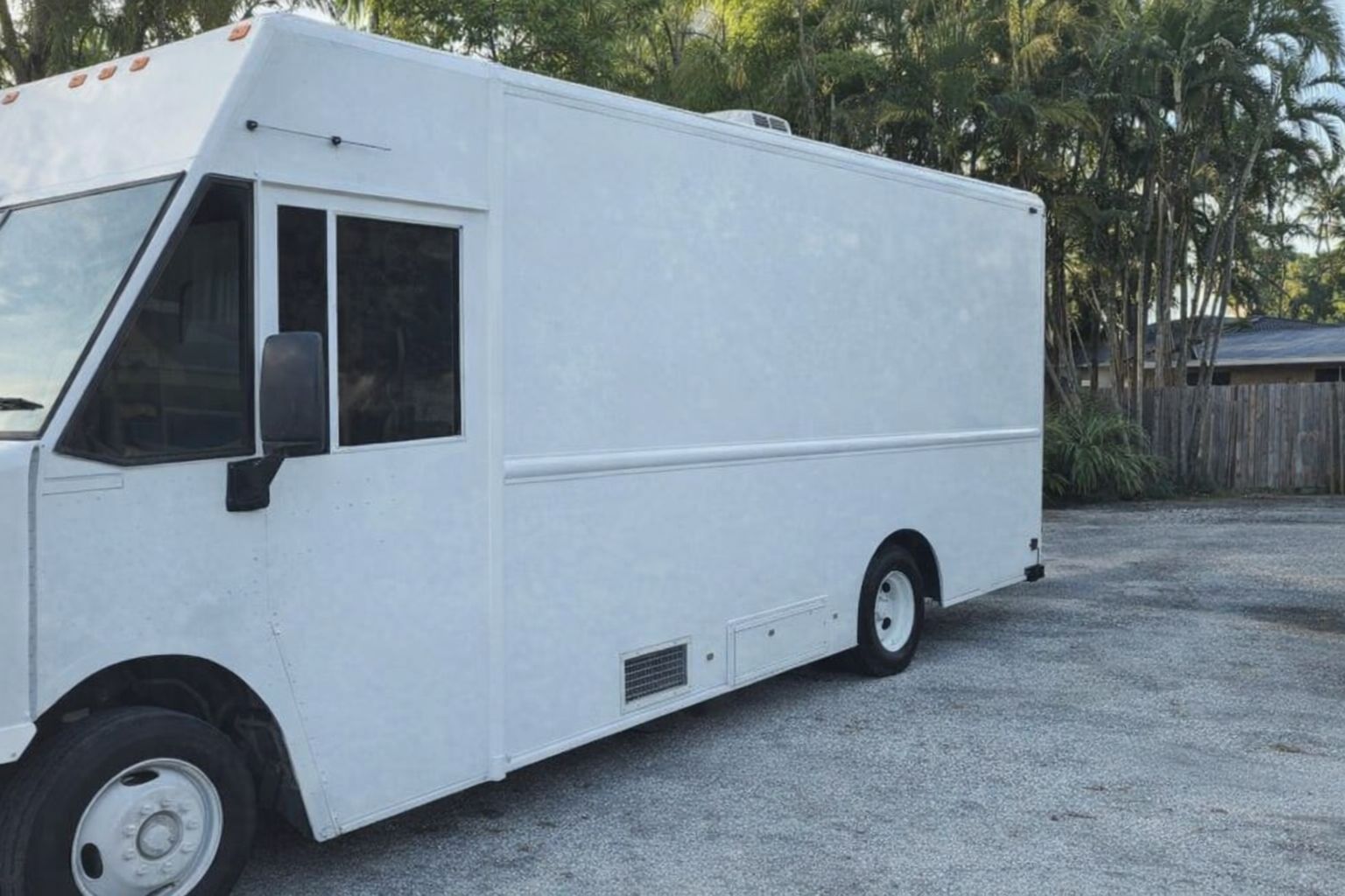 Een grote, witte bedrijfswagen geparkeerd voor een bosrijke omgeving.